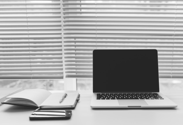 An image of a desk in front of horizontal blinds that are hung at the window.
