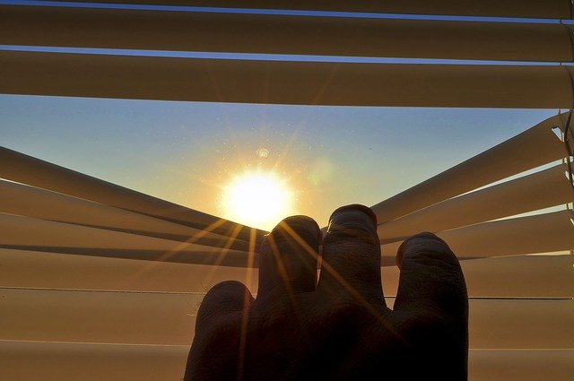 image of a hand pulling down blinds to let in sun