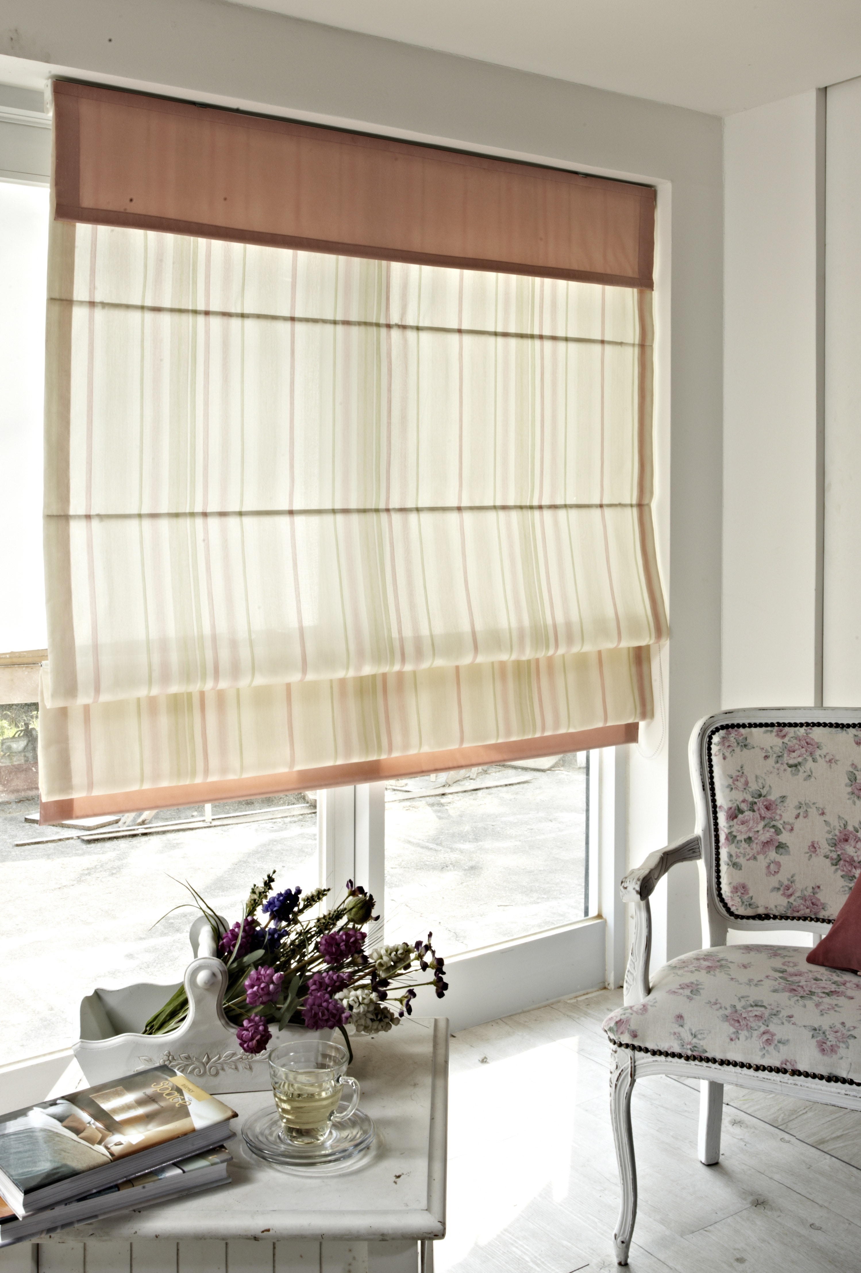 An image of a window with a beige coloured roman blind behind a coffee table and chair